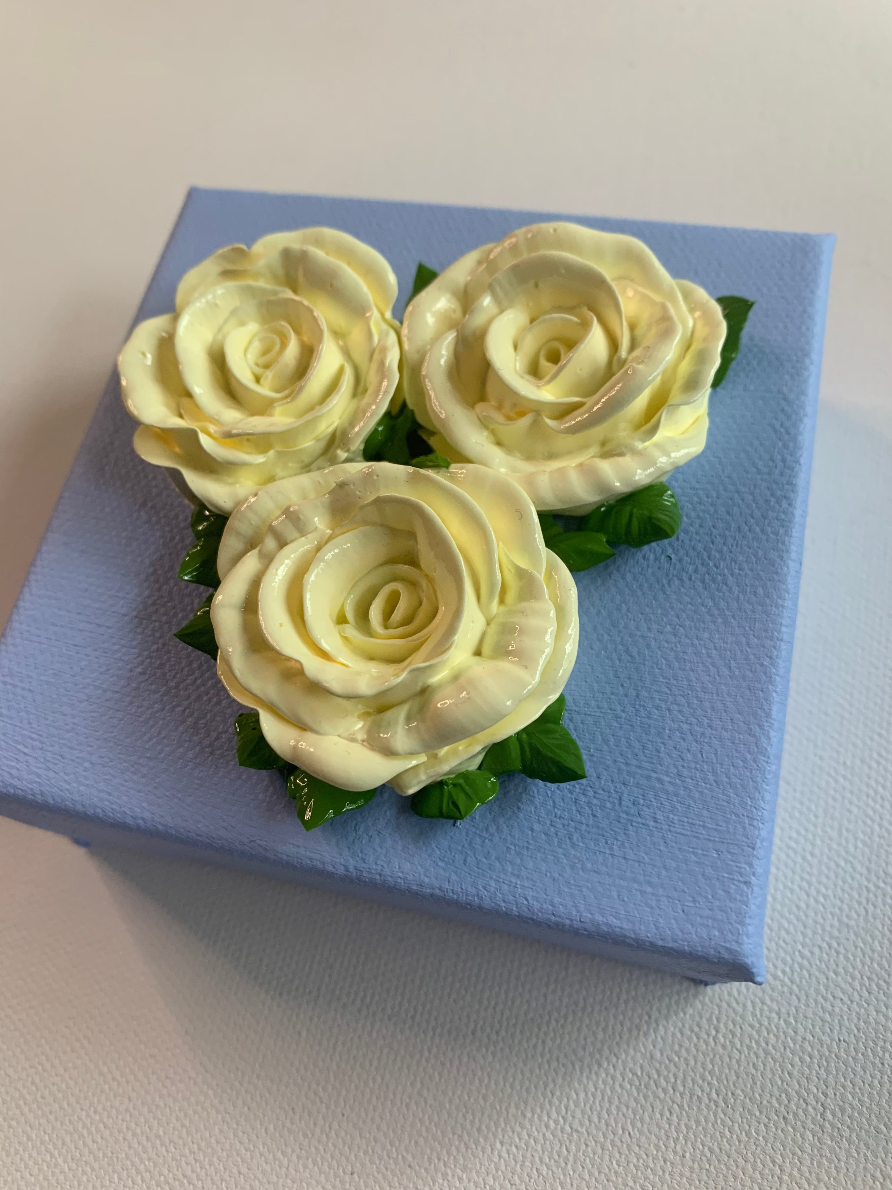 Three creamy white roses on a powder blue background, angled.