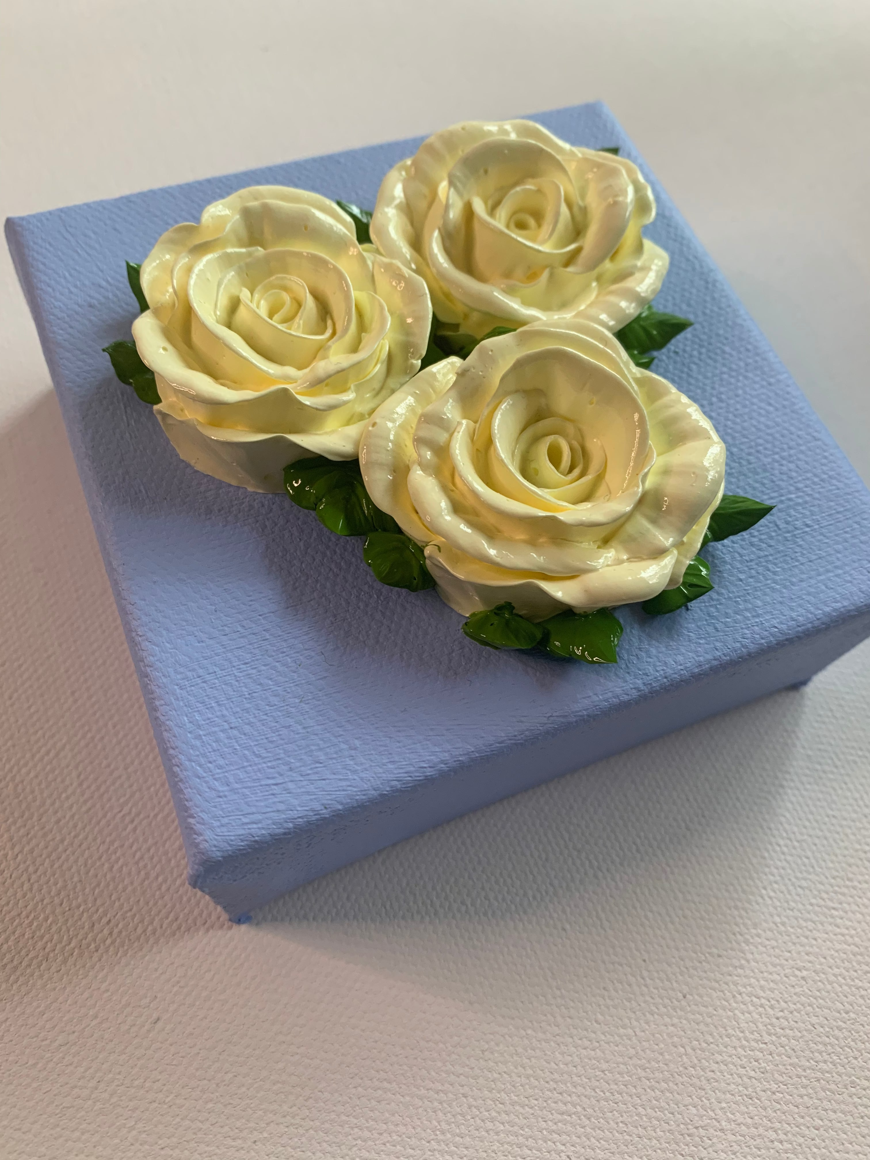 Three creamy white roses on a powder blue background, angled.